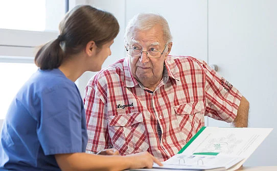 Ärztin im Gespräch mit einem älteren Patienten über medizinische Unterlagen.