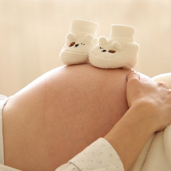 Eine schwangere Frau liegt und hat Babyschuhe auf ihrem Bauch liegen.