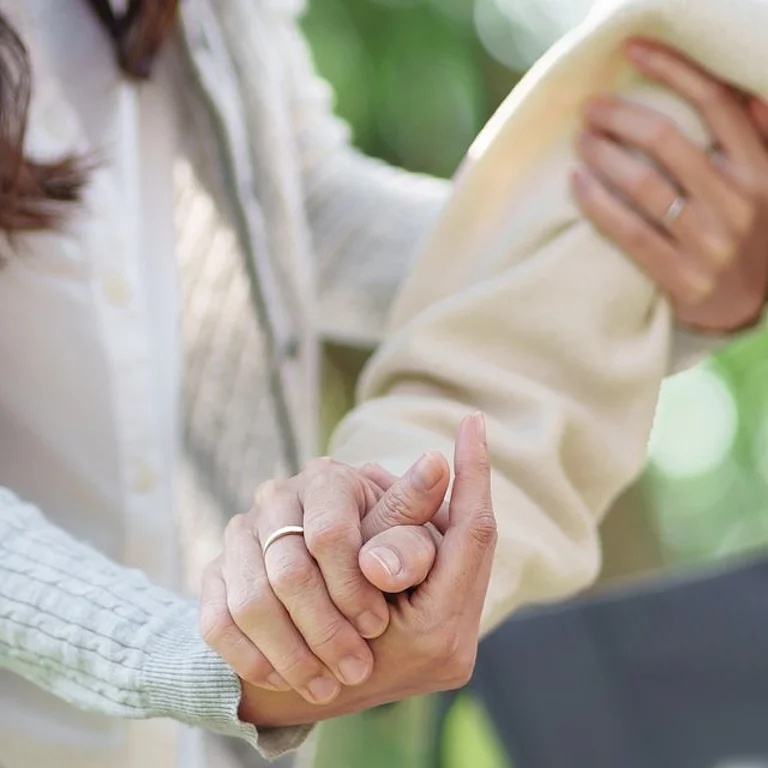 Jüngere Frau unterstützt ältere Person beim Gehen durch Halten von Arm und Hand