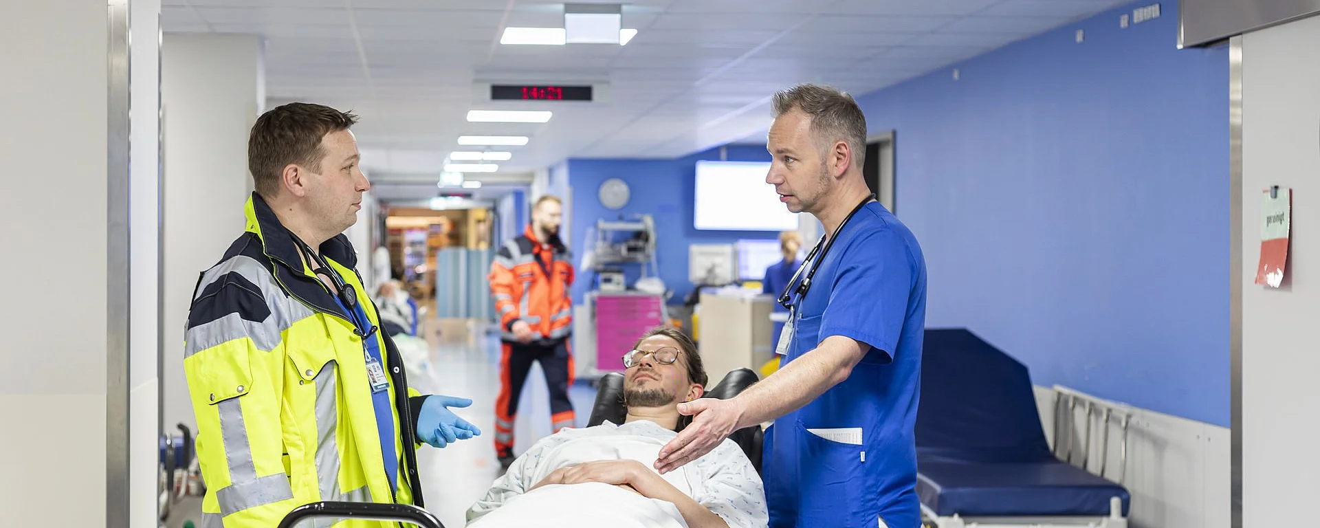 Ein Notarzt unterhält sich mit einem Pfleger. Zwischen den beiden liegt eine Patientin auf einer Trage.