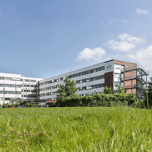 Außenansicht eines modernen Klinikgebäudes bei sonnigem Wetter, im Vordergrund eine grüne Wiese mit Bäumen.