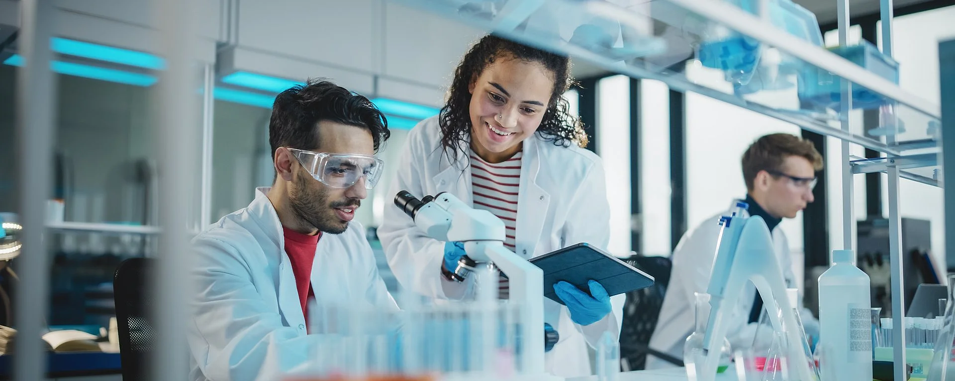Junge Forschende im Labor analysieren Proben mit Mikroskop und Tablet