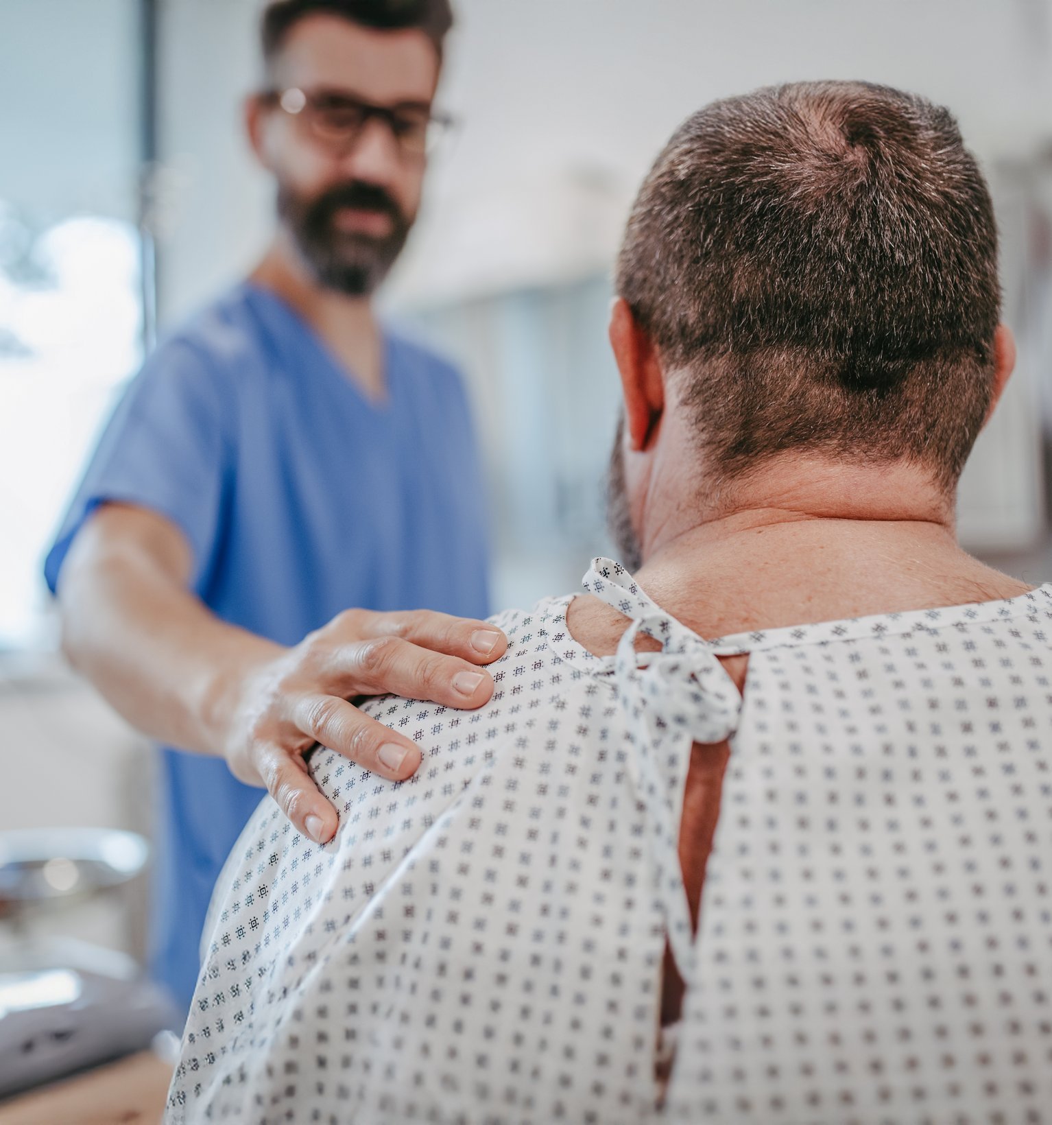 Arzt legt beruhigend die Hand auf Schulter eines männlichen Patienten im Krankenhaus