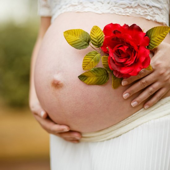 Eine Schwangere hält eine Rose neben ihrem Bauch
