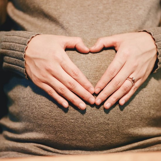 Eine schwangere Frau formt mit ihren Händen ein Herz und hält sie vor ihren Bauch.