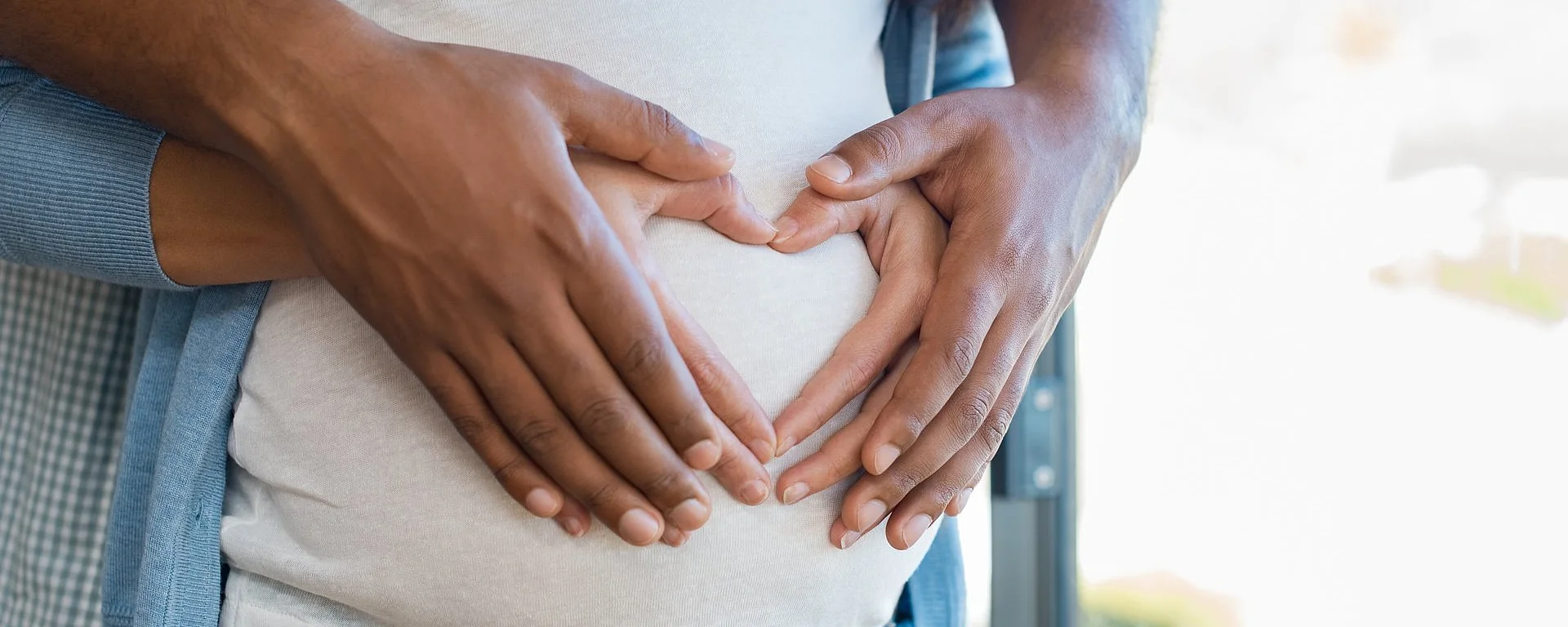 Das Bild zeigt zwei Hände, die gemeinsam ein Herz auf dem Babybauch einer schwangeren Frau formen – ein Symbol für Liebe und Vorfreude auf das Kind.