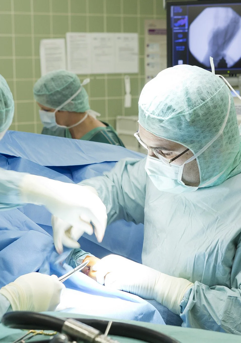 Chirurgisches Team im AKH Celle in steriler OP-Umgebung bei einer Operation mit Röntgenmonitoren im Hintergrund.