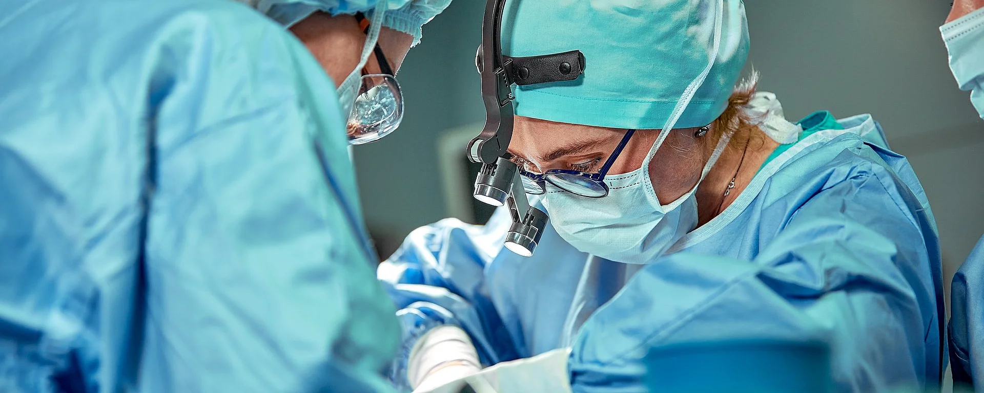Drei Chirurginnen operieren. Alle tragen steriles Gewand und Masken.