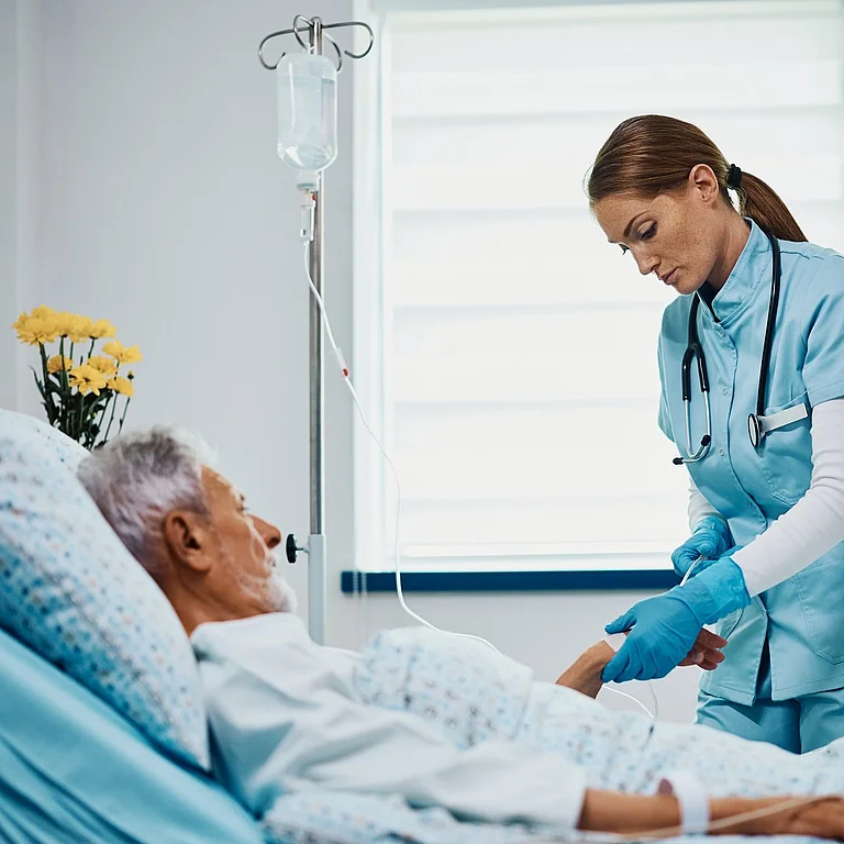 Eine Pflegerin überprüft die Infusion eines älteren Patienten, der in einem Krankenhausbett liegt.