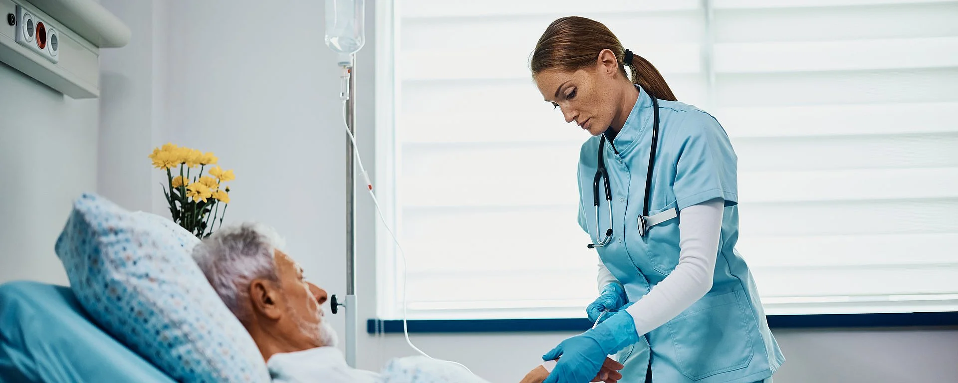 Eine Pflegerin überprüft die Infusion eines älteren Patienten, der in einem Krankenhausbett liegt.