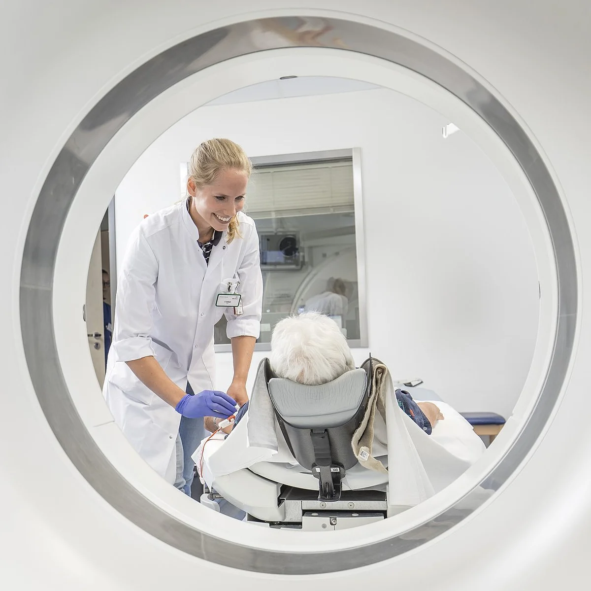 Blick durch die Öffnung eines CT-Geräts auf einen Arzt, der einen Patienten vorbereitet.