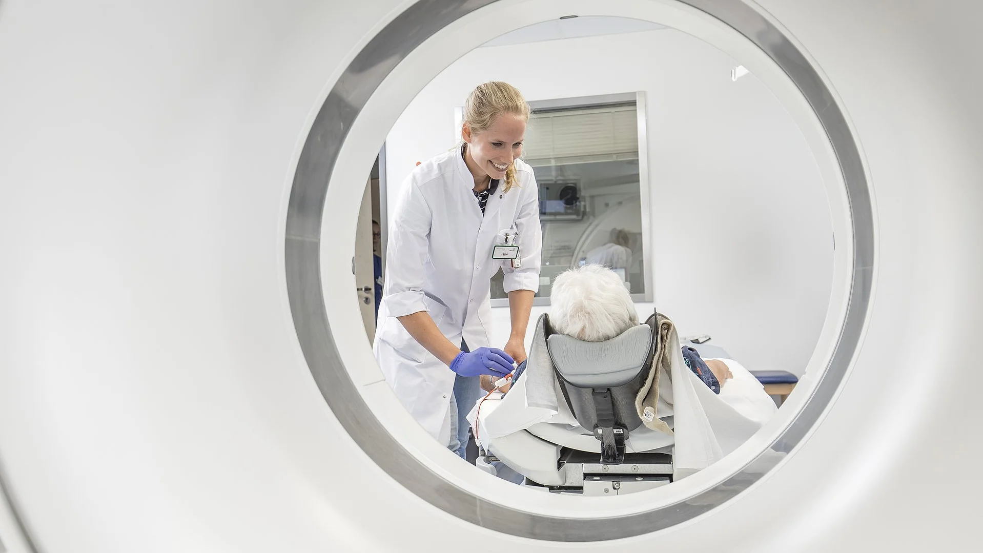 Blick durch die Öffnung eines CT-Geräts auf einen Arzt, der einen Patienten vorbereitet.