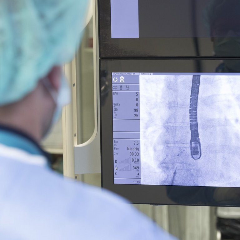 Ein Arzt schaut auf einige Monitore mit Werten und Aufnahmen des Herzens.