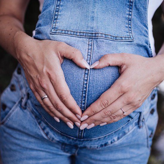 Schwangere Frau formt ihre Hände zu einem Herzen und hält sie vor ihren Bauch.