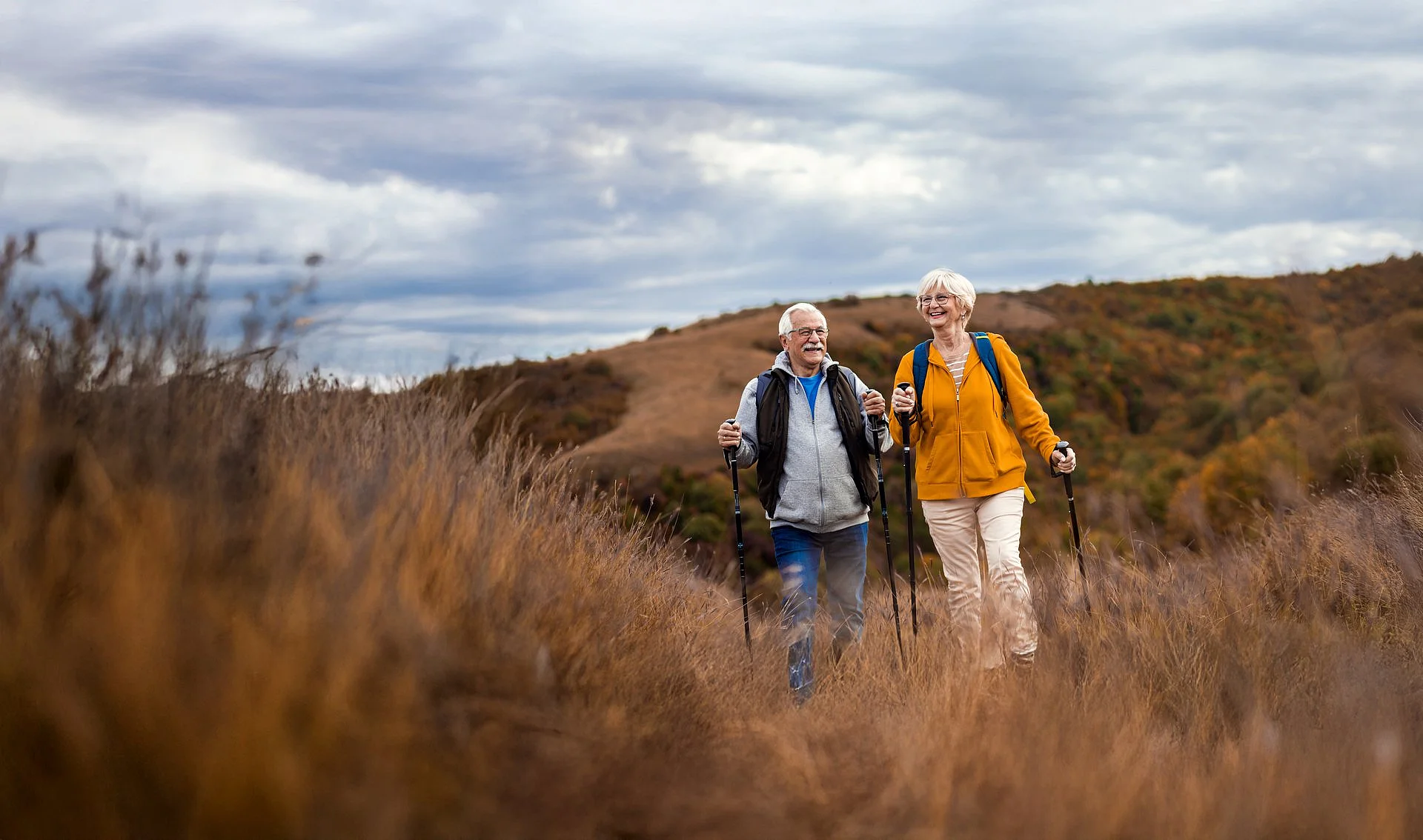Älteres Paar beim Wandern mit Trekkingstöcken in herbstlicher Hügellandschaft