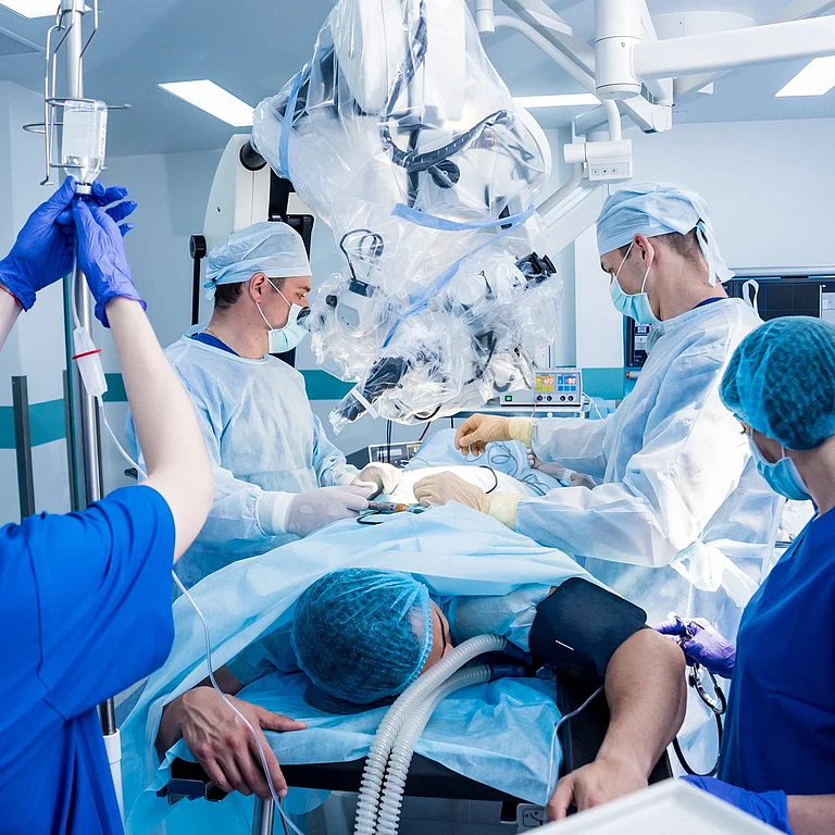Operationsteam bei einem chirurgischen Eingriff unter OP-Leuchten und Mikroskop.
