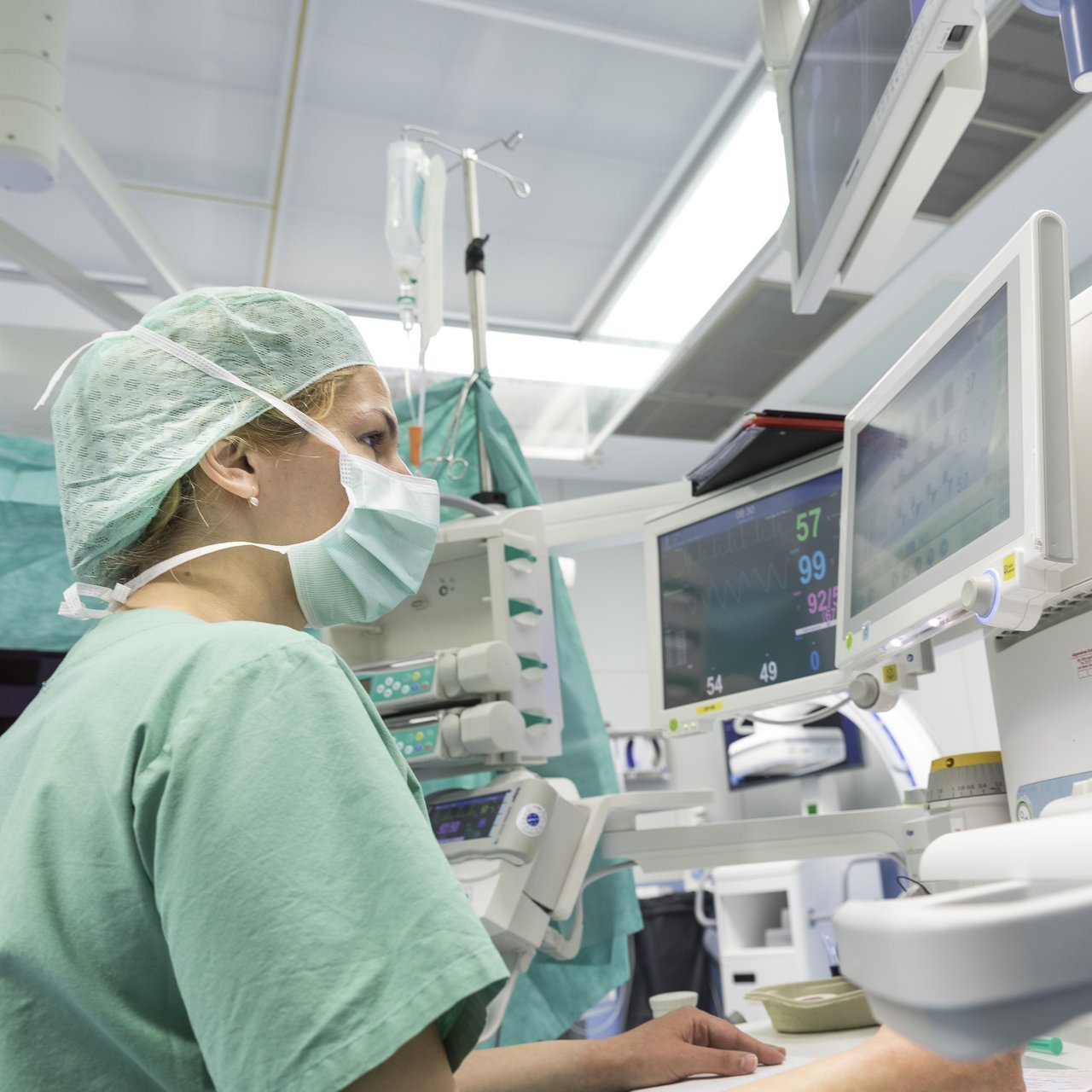 Anästhesistin überwacht die Vitalfunktionen eines Patienten an mehreren Monitoren im OP.