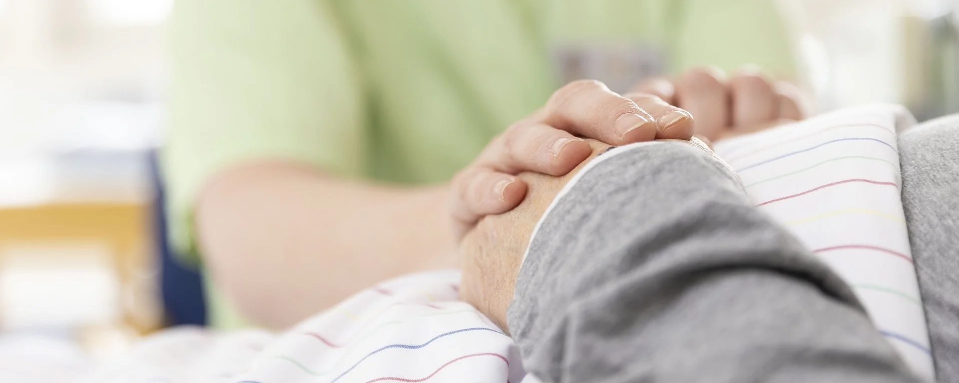 Eine Pflegekraft hält einfühlsam die Hand einer liegenden Person – ein Moment der Fürsorge und menschlichen Nähe.
