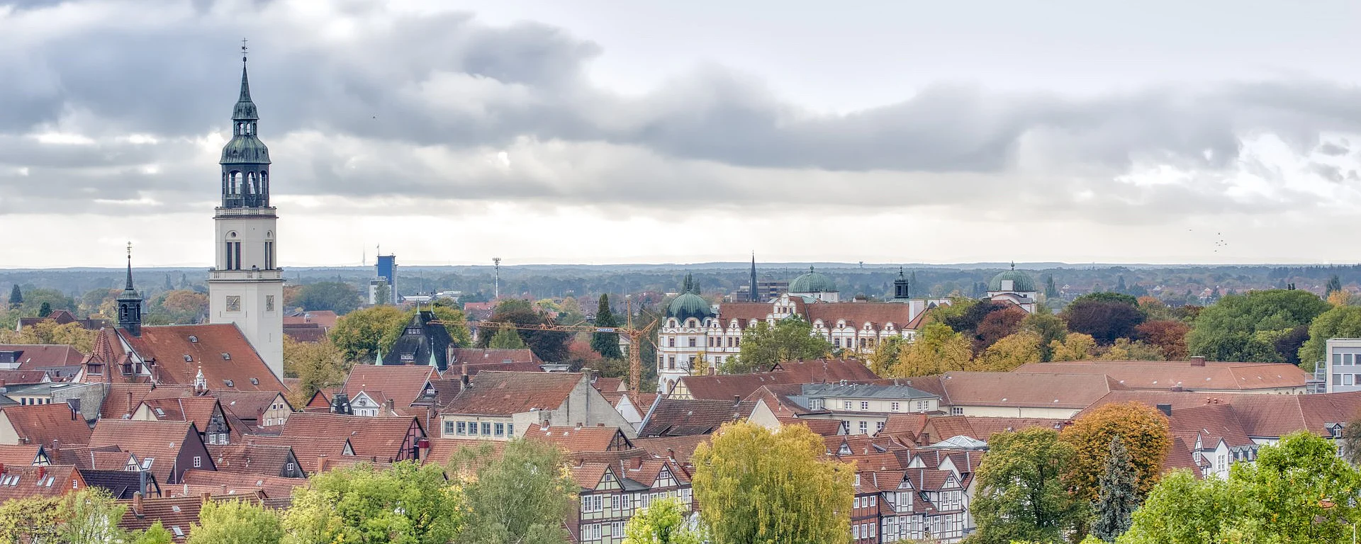 Blick über Celle mit roten Dächern und herbstlich gefärbten Bäumen, im Hintergrund ein markanter Kirchturm. Die Stimmung wirkt ruhig und malerisch.