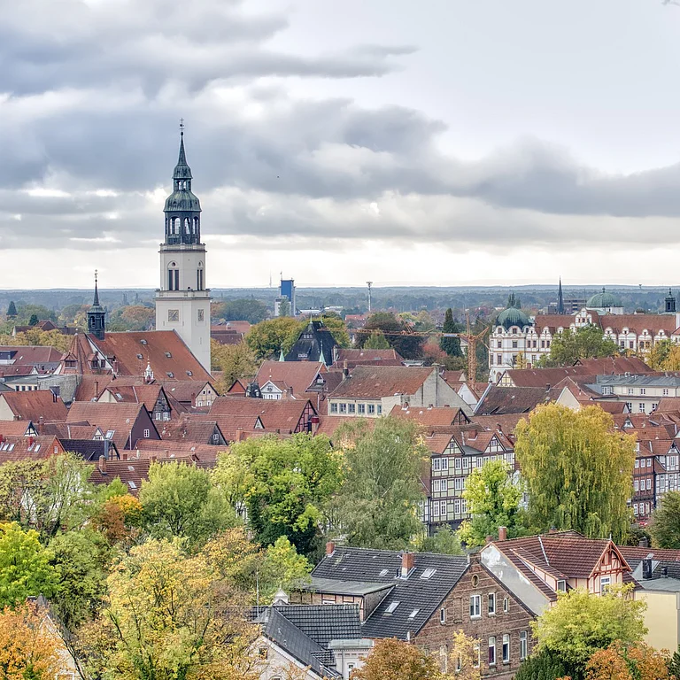 Blick über Celle mit roten Dächern und herbstlich gefärbten Bäumen, im Hintergrund ein markanter Kirchturm. Die Stimmung wirkt ruhig und malerisch.
