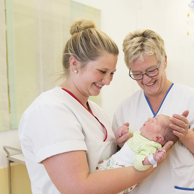 Zwei Pflegekräfte in der Neugeborenenstation halten gemeinsam ein Baby im Arm.