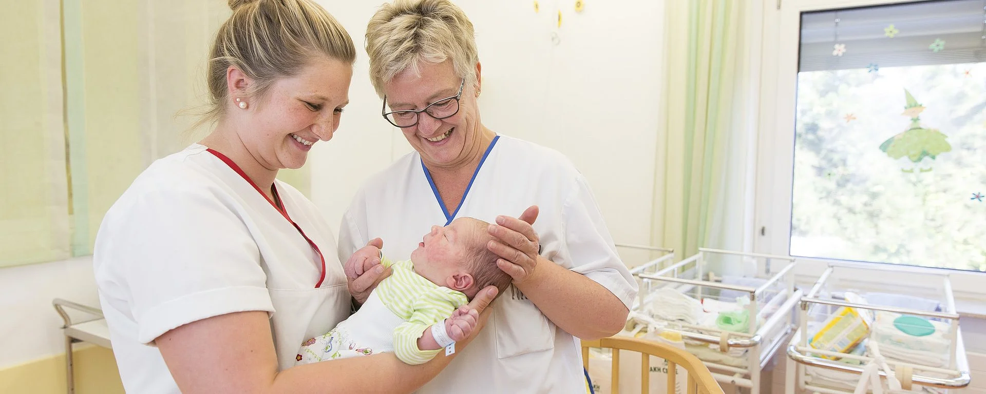 Zwei Pflegekräfte in der Neugeborenenstation halten gemeinsam ein Baby im Arm.