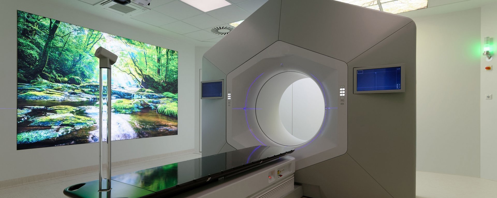 Moderner Behandlungsraum mit großem Strahlentherapiegerät und beruhigender Naturprojektion an der Wand.