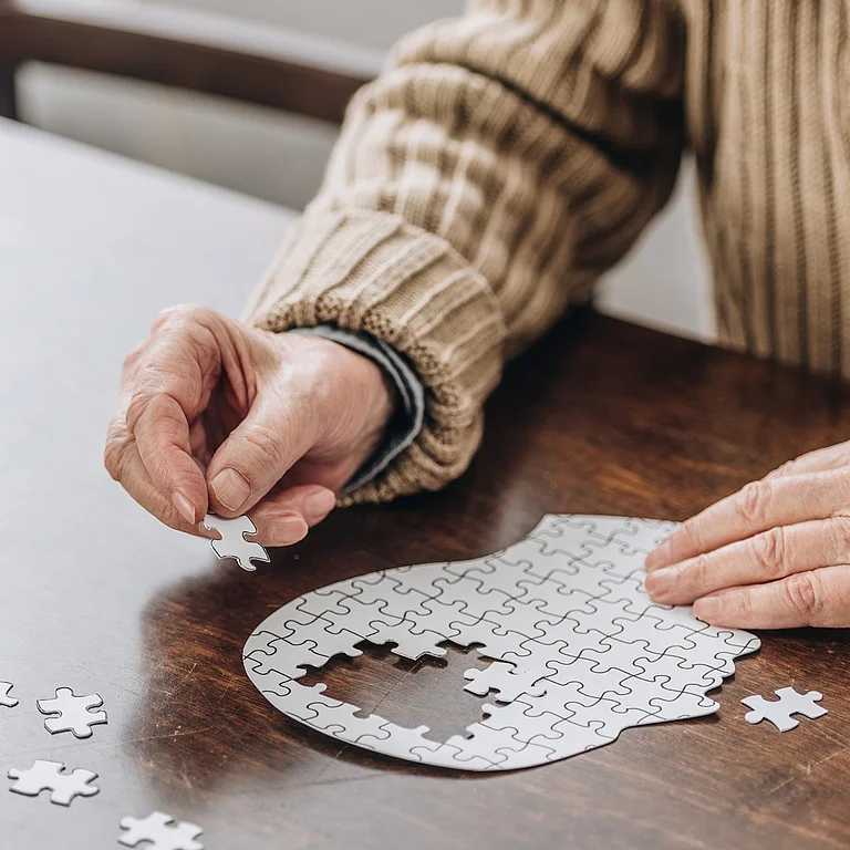 Ältere Person setzt Puzzleteil in Kopfform zur Symbolisierung von Demenz oder Gedächtnistraining