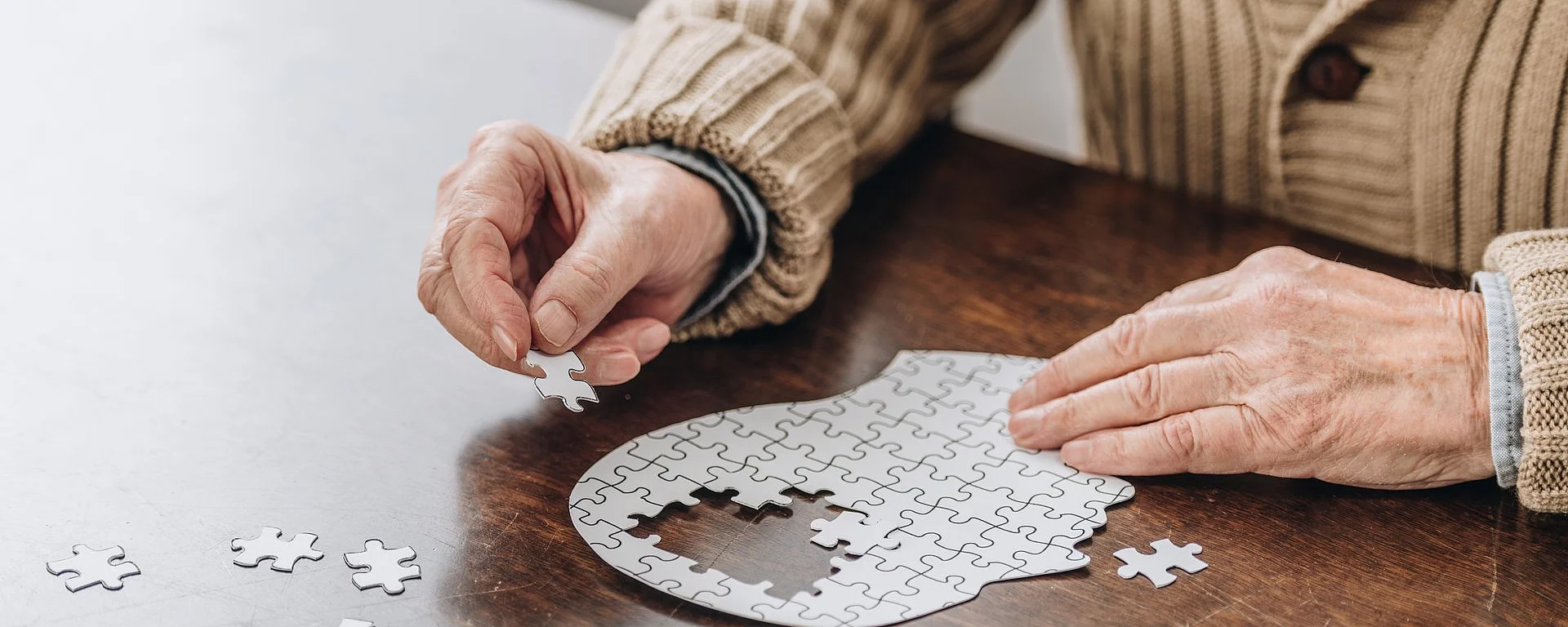 Ältere Person setzt Puzzleteil in Kopfform zur Symbolisierung von Demenz oder Gedächtnistraining
