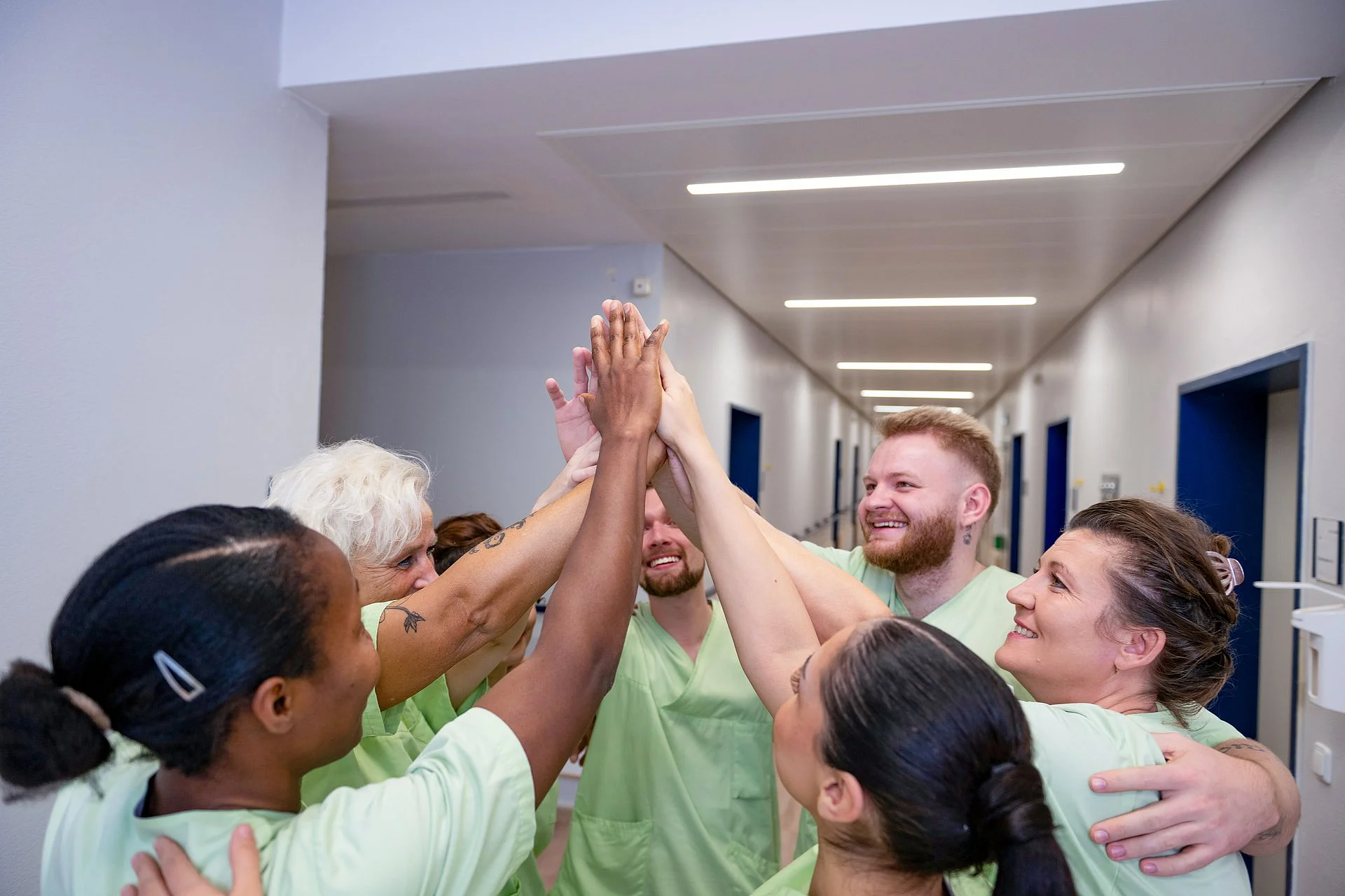 Pflegeteam steht im Kreis und legt im Flur motiviert die Hände zu einem High Five zusammen.