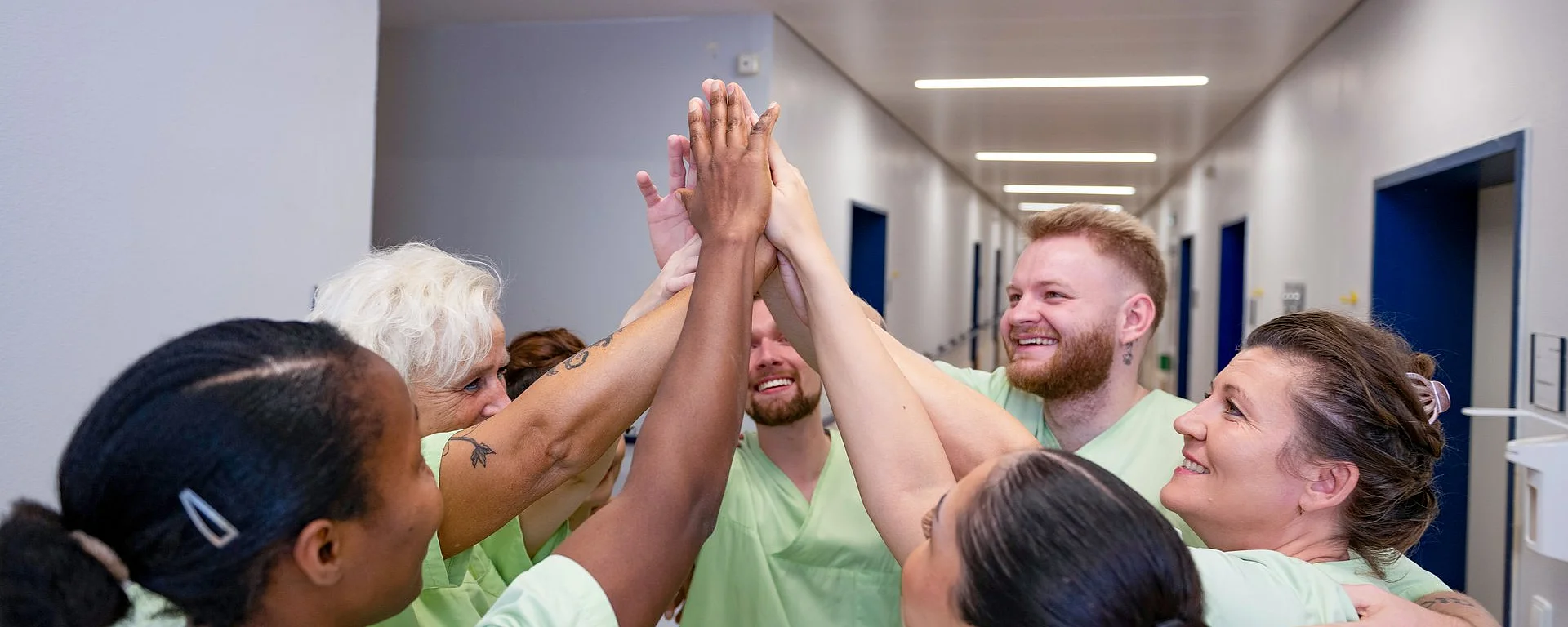 Pflegeteam steht im Kreis und legt im Flur motiviert die Hände zu einem High Five zusammen.