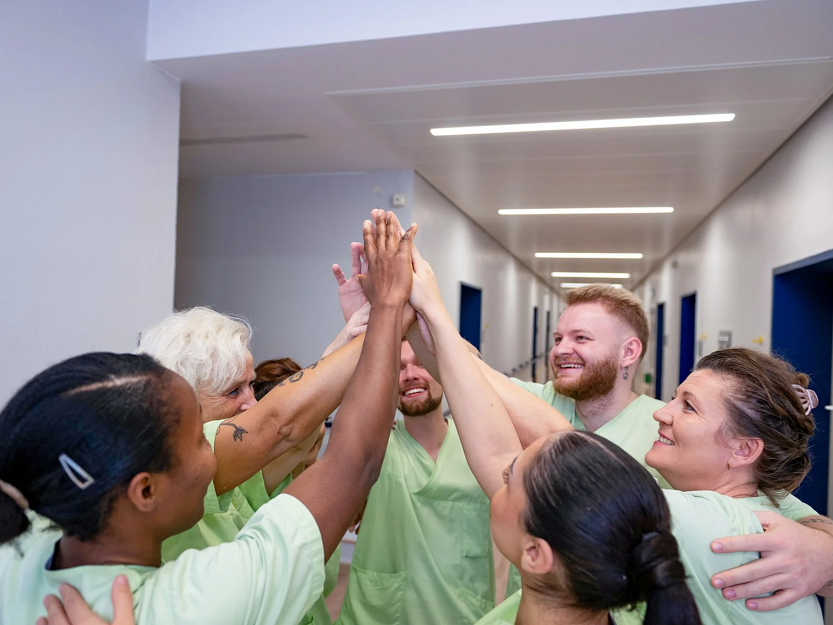 Pflegeteam steht im Kreis und legt im Flur motiviert die Hände zu einem High Five zusammen.