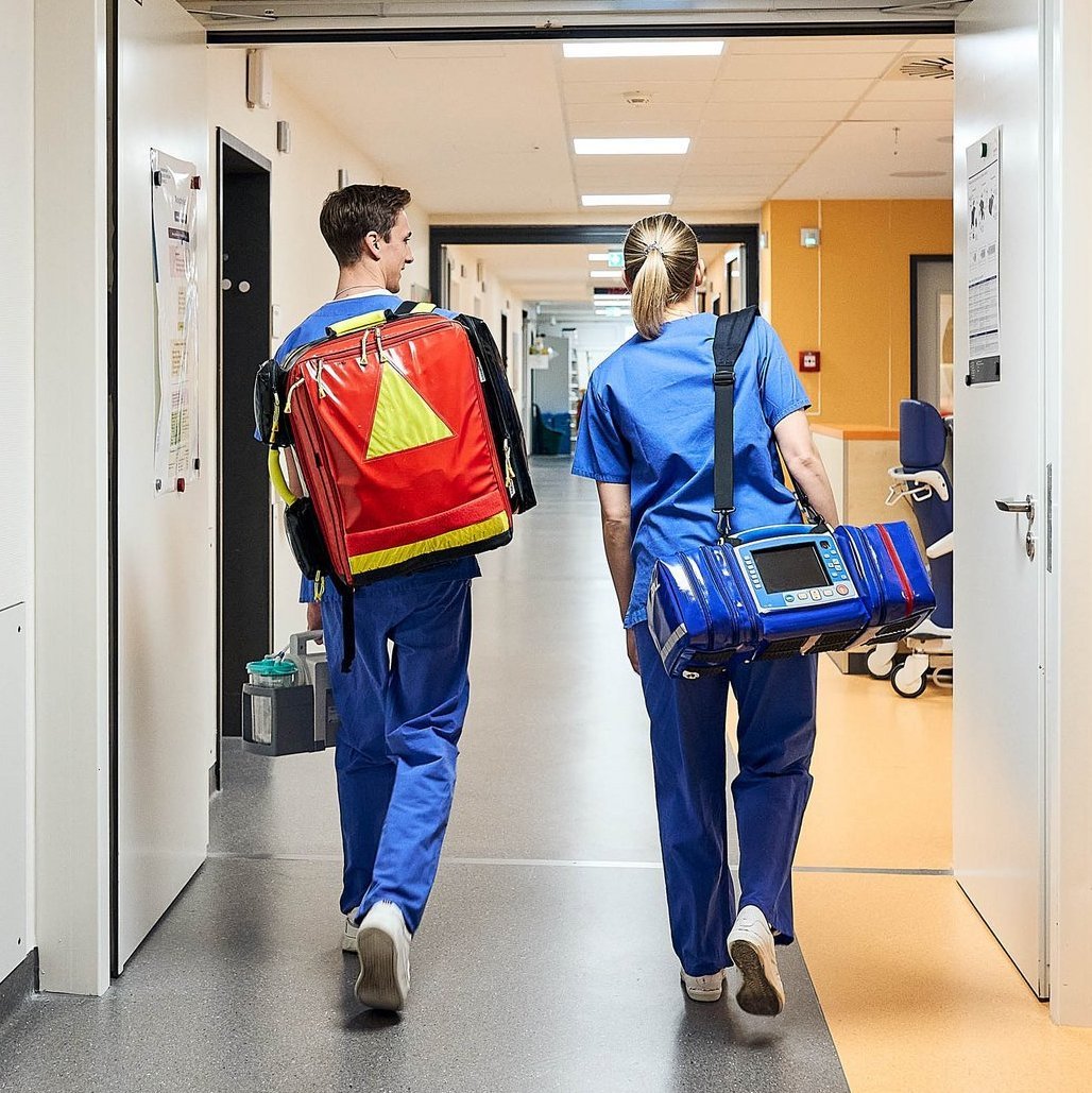 Zwei Notfallsanitäter mit Ausrüstung gehen durch den Flur der ZNA in Richtung Ausgang.