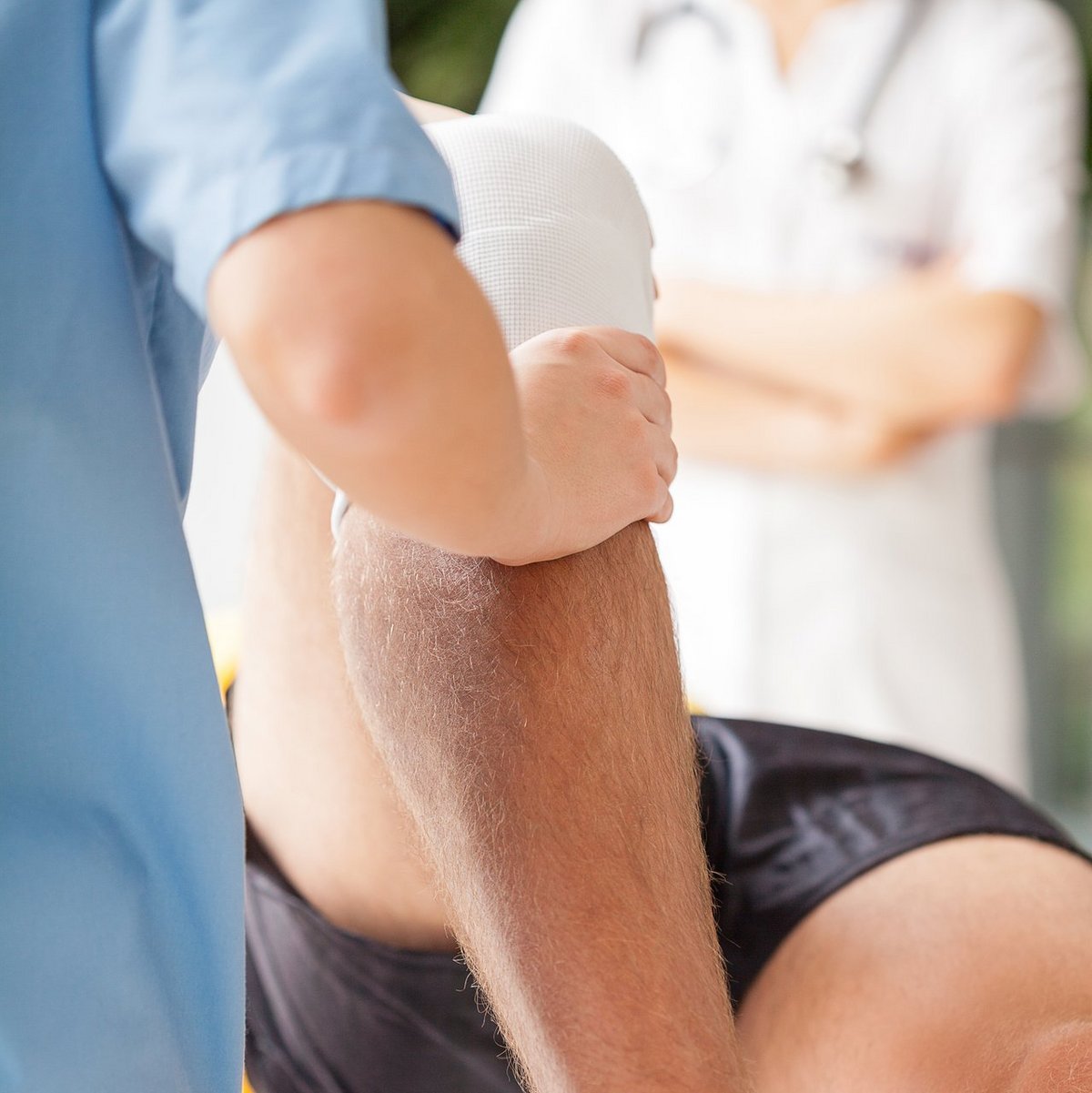 Physiotherapeutin mobilisiert bandagiertes Knie eines männlichen Patienten während Rehabilitationsbehandlung