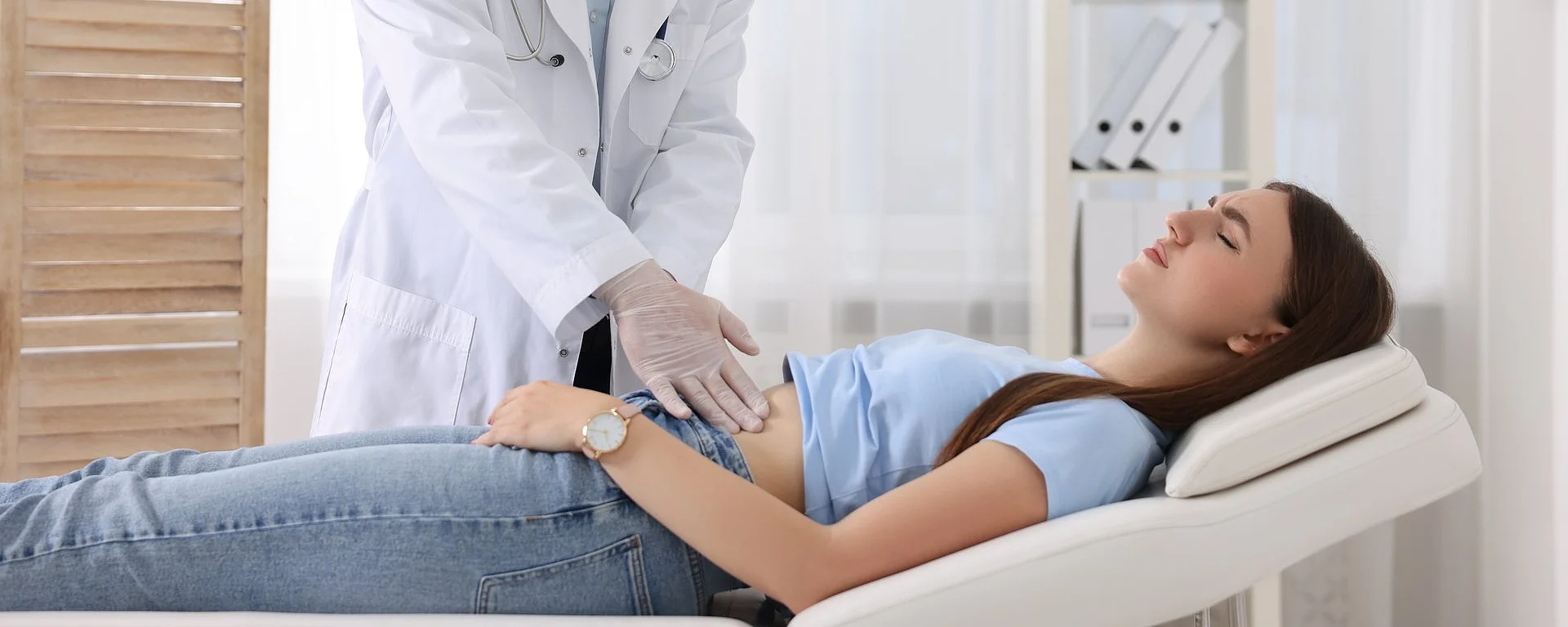 Arzt tastet Bauch einer jungen Frau während Untersuchung im Behandlungszimmer ab