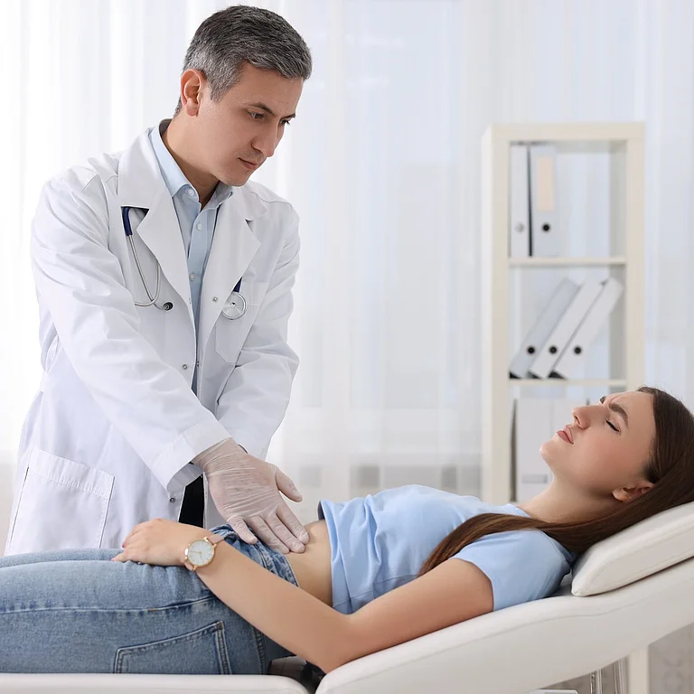 Arzt tastet Bauch einer jungen Frau während Untersuchung im Behandlungszimmer ab