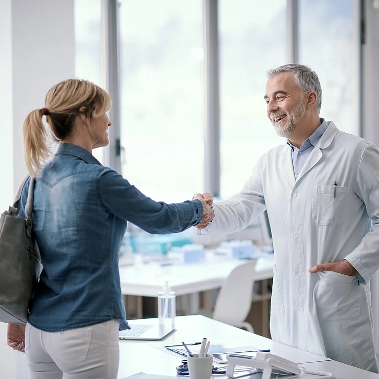 Arzt begrüßt Patientin mit Handschlag im modernen Behandlungszimmer