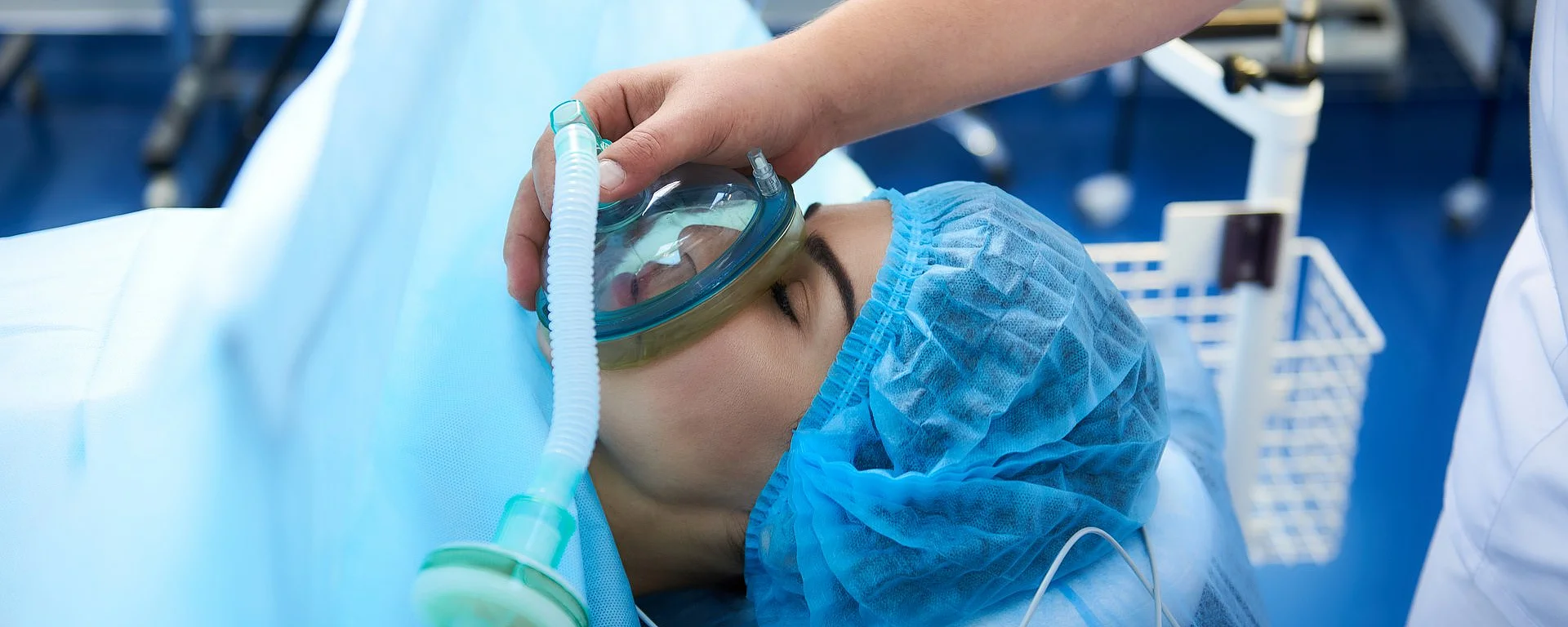 Ein Patient wird im Operationssaal für eine Narkose vorbereitet. Eine medizinische Fachkraft hält ihm eine Beatmungsmaske über Mund und Nase.