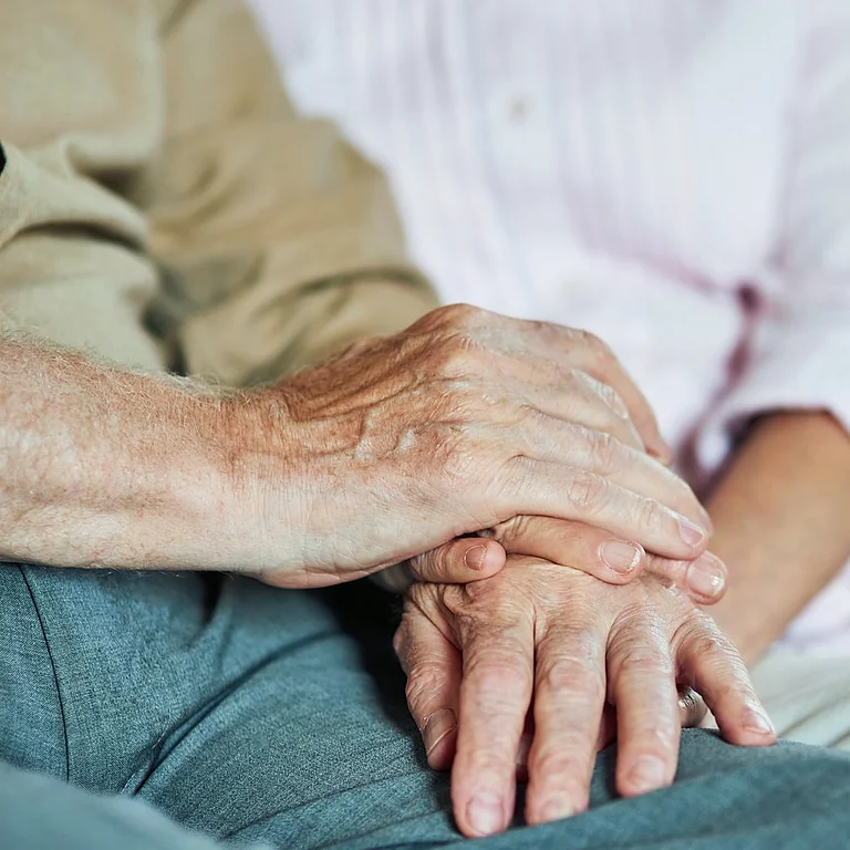 Älteres Paar hält sich liebevoll an den Händen auf dem Sofa