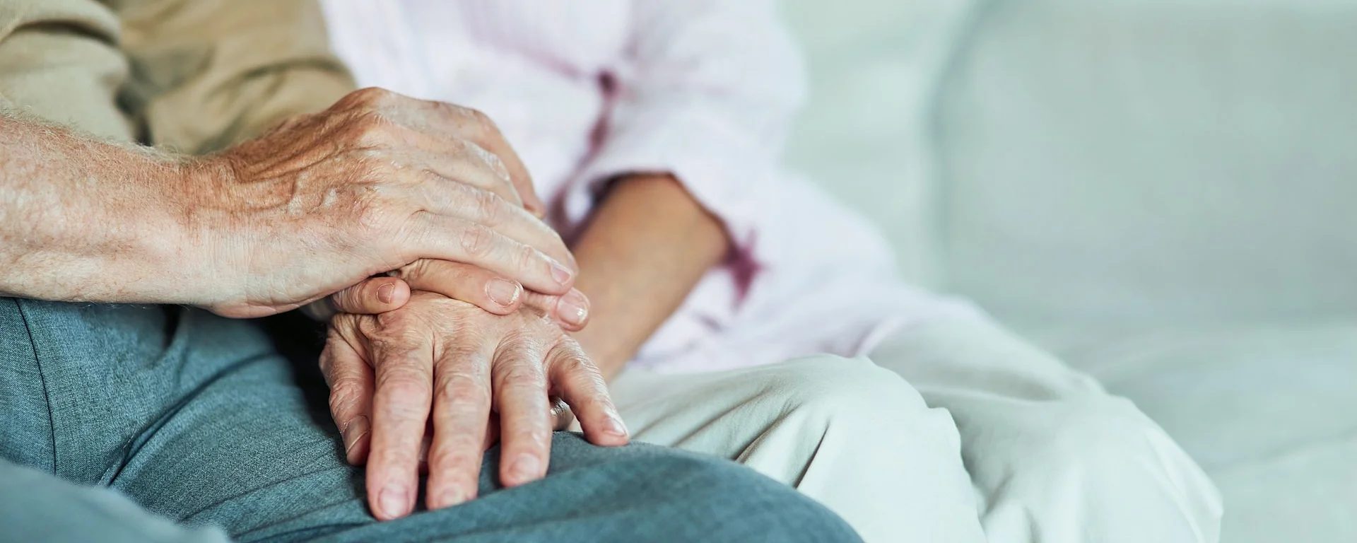 Älteres Paar hält sich liebevoll an den Händen auf dem Sofa