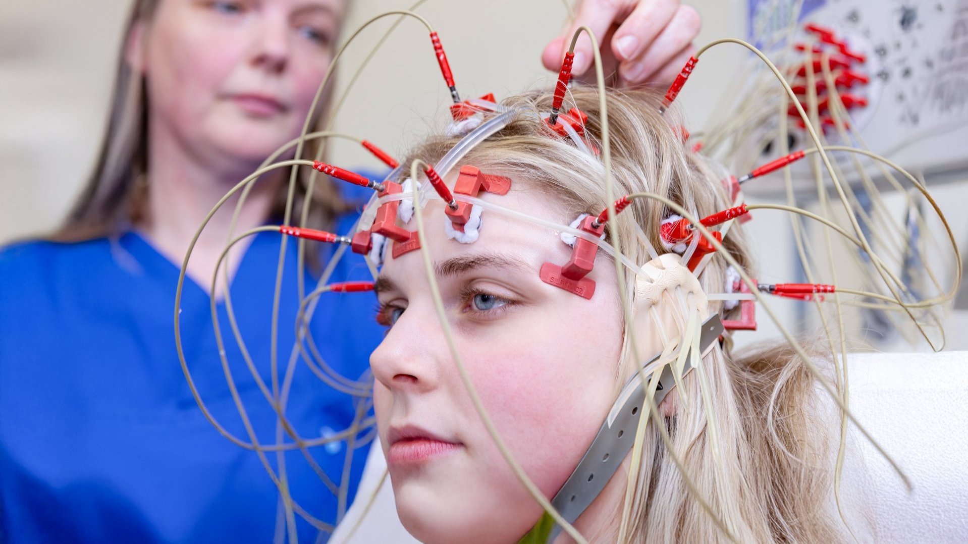Medizinische Fachkraft befestigt EEG-Elektroden an der Stirn einer jungen Patientin.
