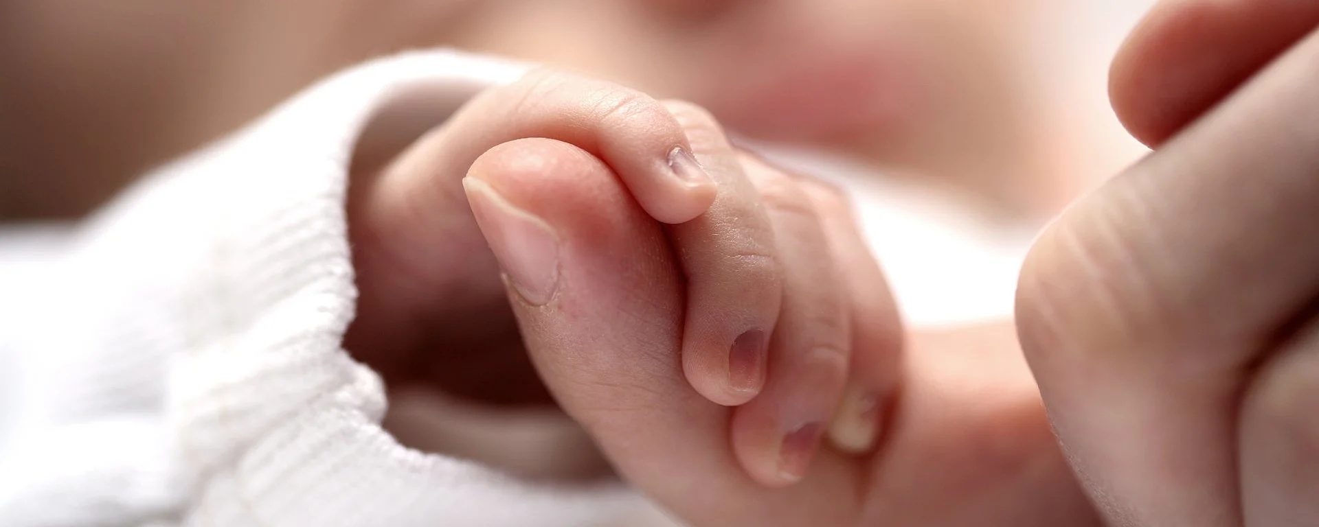 Neugeborenes hält Finger eines Erwachsenen als Symbol für Bindung und Geborgenheit