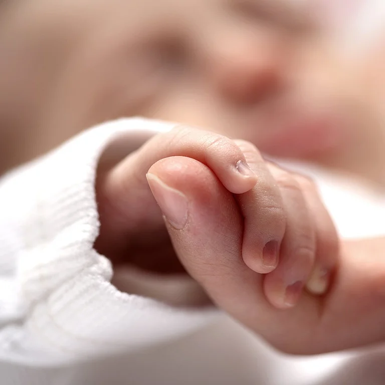 Neugeborenes hält Finger eines Erwachsenen als Symbol für Bindung und Geborgenheit