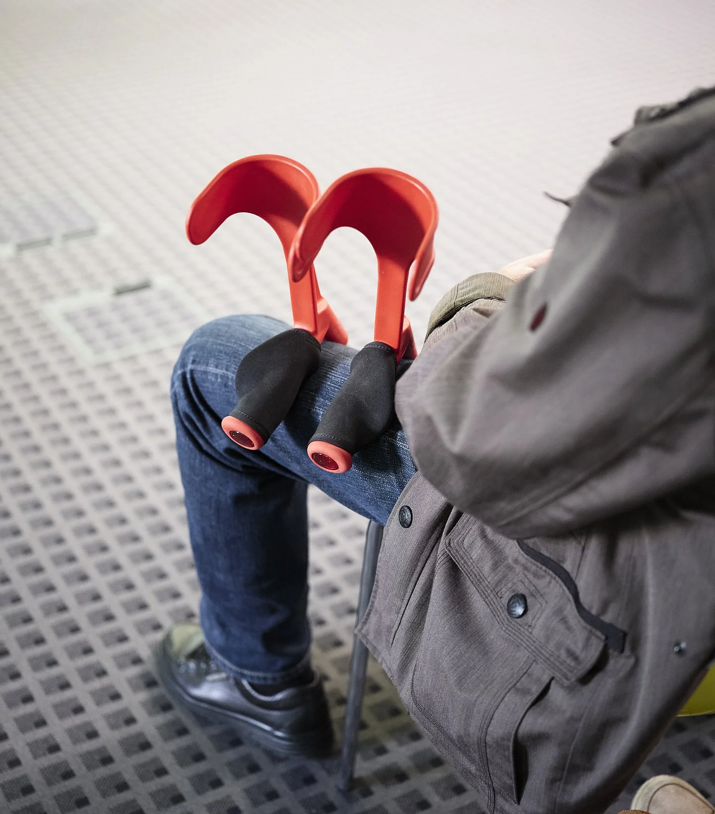 Zusammengefaltete rote Unterarmgehstützen liegen auf dem Schoß einer sitzenden Person.