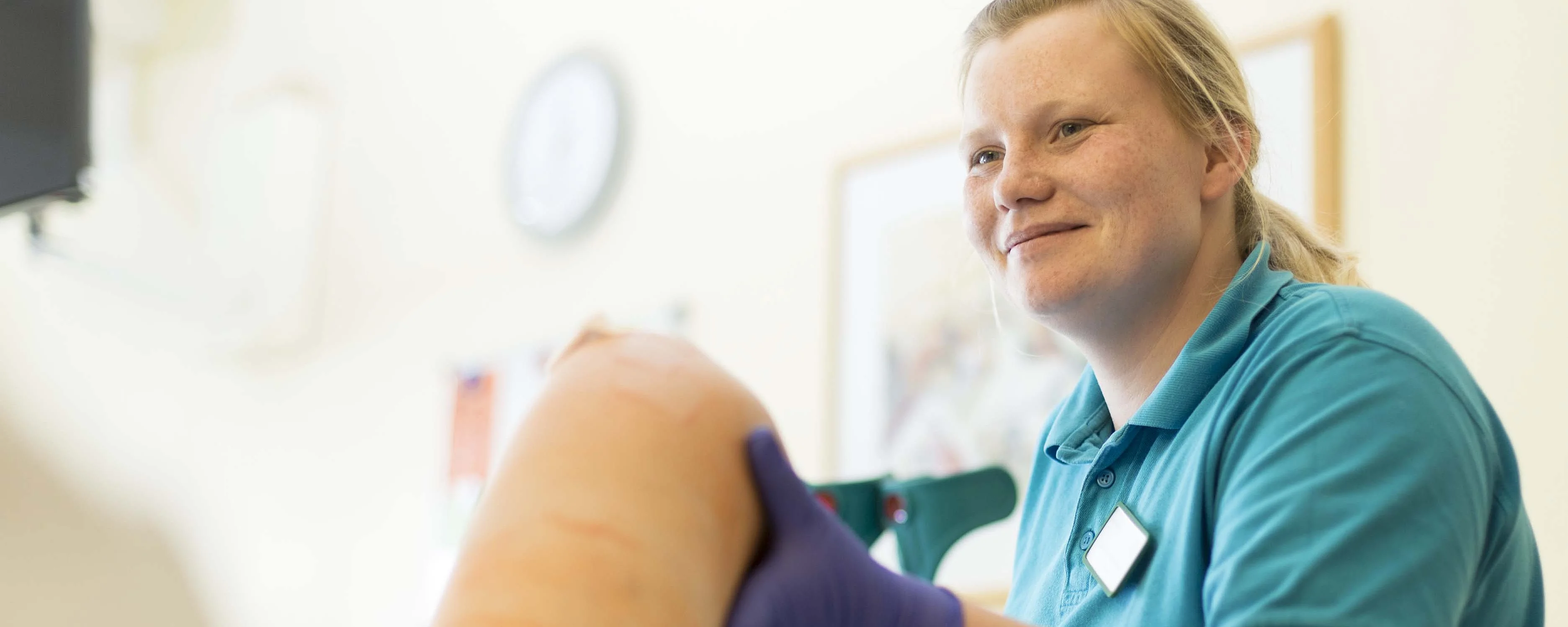 Pflegekraft untersucht das Knie einer Patientin im Behandlungszimmer.