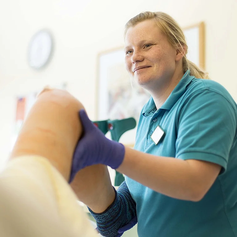 Pflegekraft untersucht das Knie einer Patientin im Behandlungszimmer.