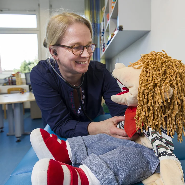 Therapeutin spielt mit einer Handpuppe in einem freundlich eingerichteten Kindertherapieraum.