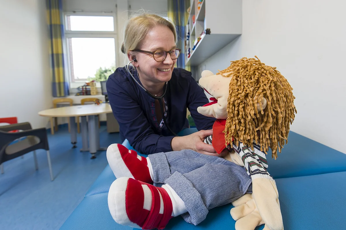 Therapeutin spielt mit einer Handpuppe in einem freundlich eingerichteten Kindertherapieraum.