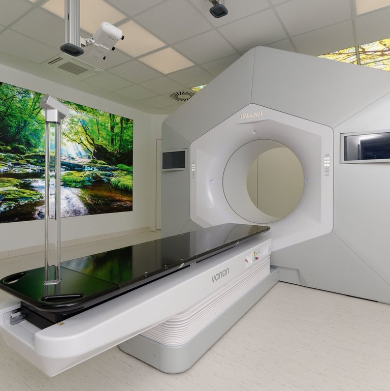 Gerät zur Strahlentherapie steht in einem Raum in dem im Hintergrund ein Landschaftsbild an der Wand hängt.