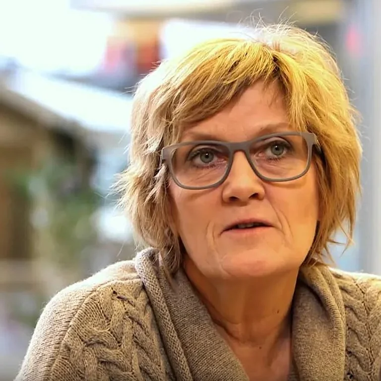 Eine ältere Frau mit hellen Haaren schaut in die Kamera.